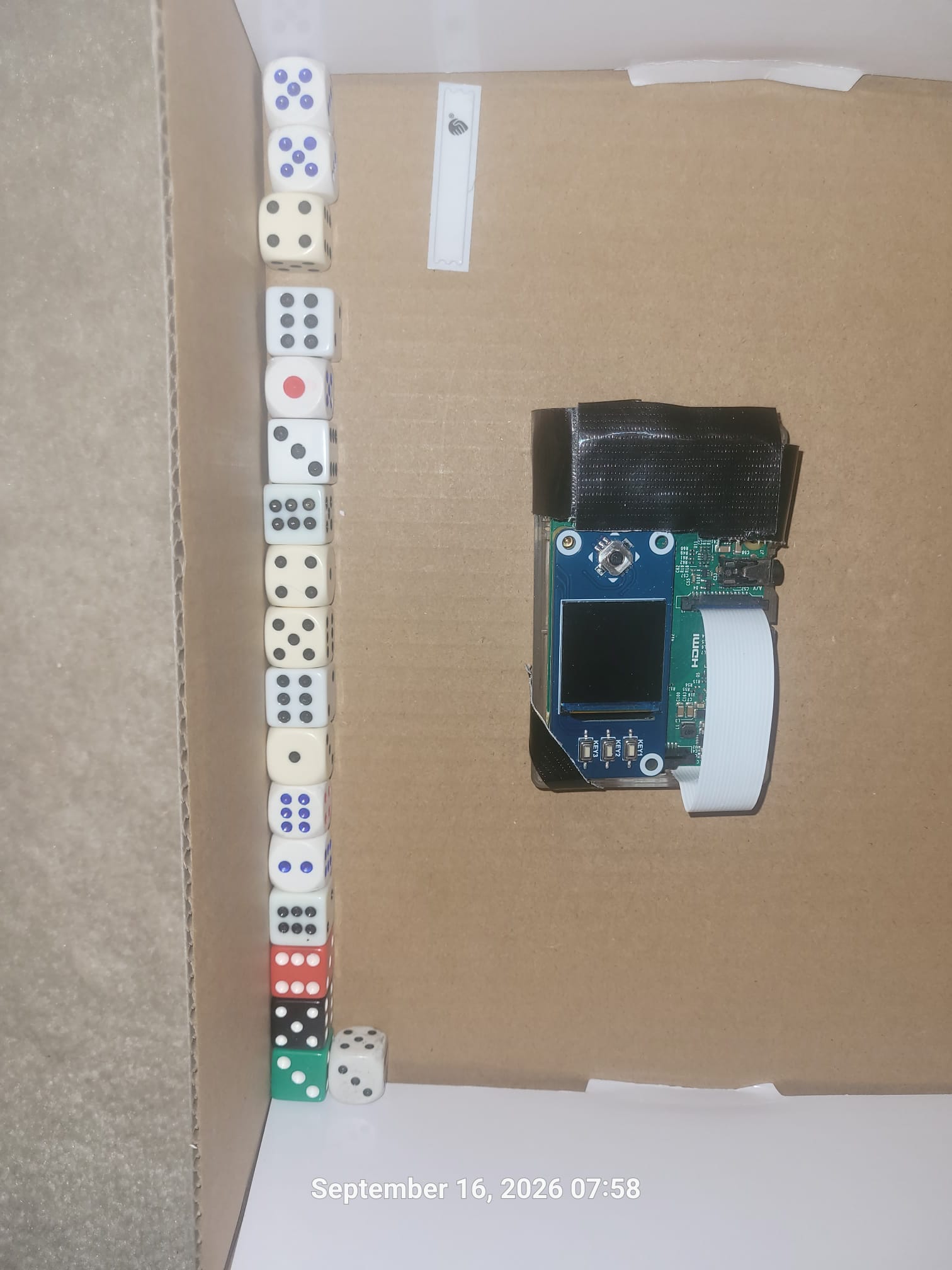 Ted Lee's open cardboard mixing box containing ordinary six-sided dice and a SeedSigner device before the device is removed for shaking